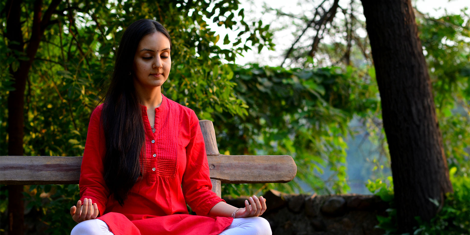 A young woman meditating on a bench in the woods