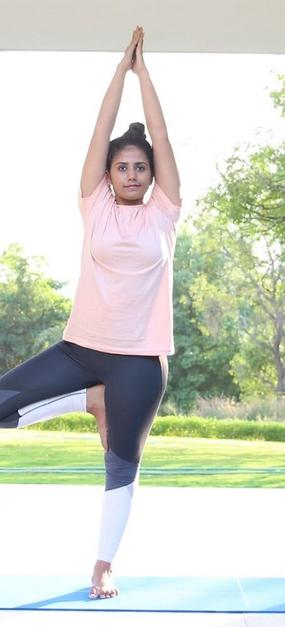 Yoga Vrikshasana - a girl standing with folded hands and one leg bent in tree pose